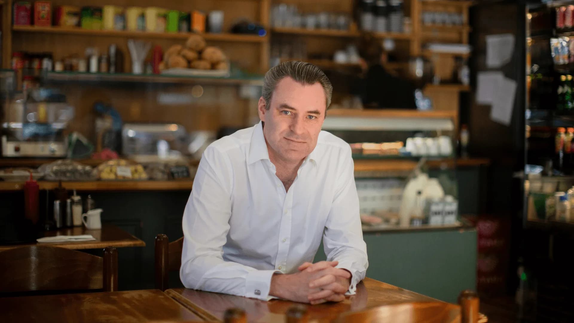 Greg Marsh, founder and CEO of Nous, sitting at a cafe table in a white shirt